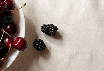 Macro shot of fresh ripe sweet cherries and blackberries in a bowl under bright sunlight with natural shadows. © Svetlana