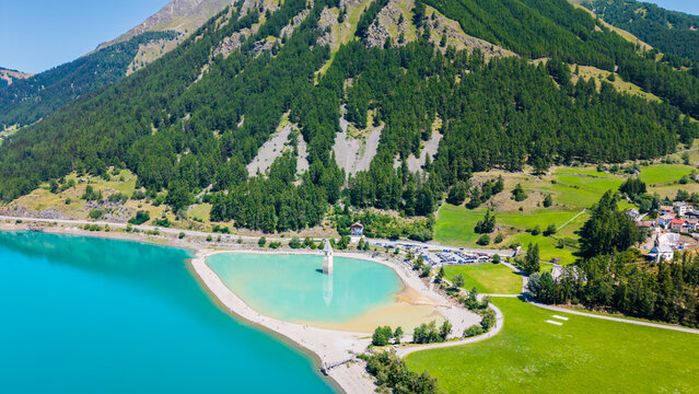 Aerial vista showing Lake Resia submerged church tower nestled beneath high pine forest mountain slopes in South Tyrol, Italy