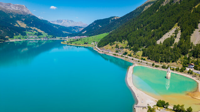 Lake Resia aerial drone vista showing turquoise reservoir basin and submerged church tower framed by alpine mountains in Curon Venosta, South Tyrol, Italy