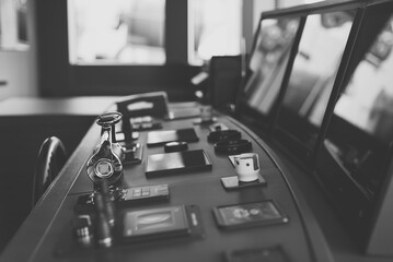 Black and white photo of wheelhouse, bridge of a modern new build superyacht, with wooden wheel, throttle controls, radar, auto-pilot, navigation and other control panels © lupiphoto