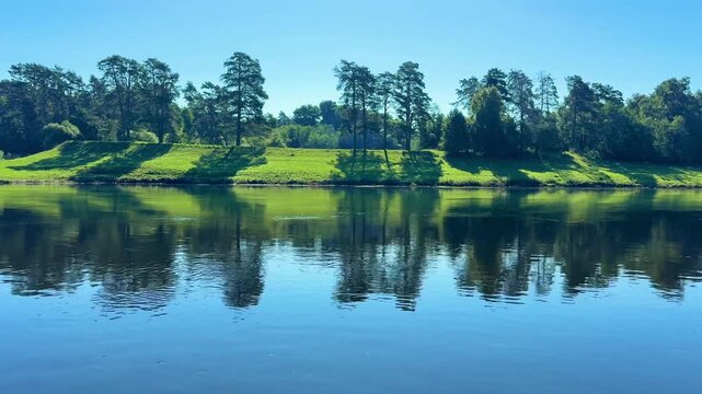 Reflections of tree line on clear river surface under bright blue sky during summer season