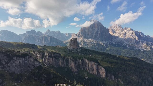Aerial drone view of Cinque Torri rising above rugged limestone cliffs and alpine forest, with the imposing Tofane massif and surrounding Dolomite peaks