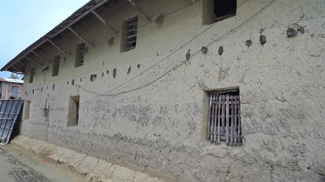 Traditional mud house exterior with rustic wooden window grilles in a rural village setting.