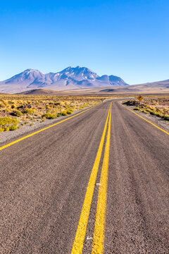 View of the Atacama Desert with a long asphalt road stretching towards distant mountains under a clear blue sky in Antofagasta, Antofagasta, Chile.