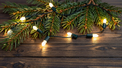 Fototapeta premium Warm glowing Christmas lights woven through evergreen branches on a rustic wooden table