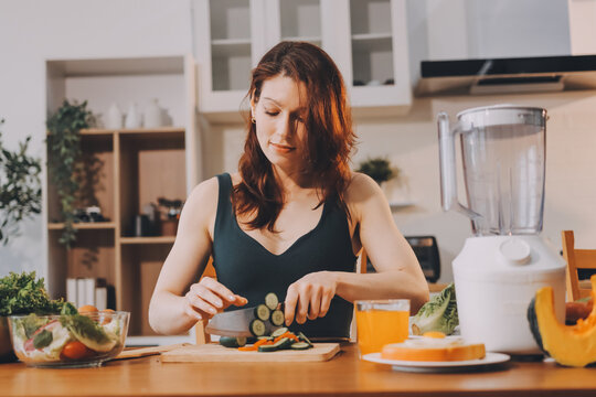 Woman preparing green smoothie in bright kitchen with fresh fruits and vegetables, healthy eating lifestyle moment in natural daylight