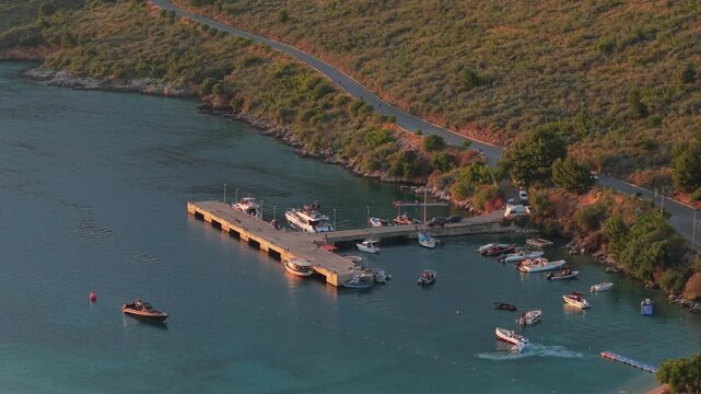 Aerial view of boats docked at a pier in Porto Palermo with a coastal road winding along the hillside in Porto Palermo, Qarku i Vlores, Albania.