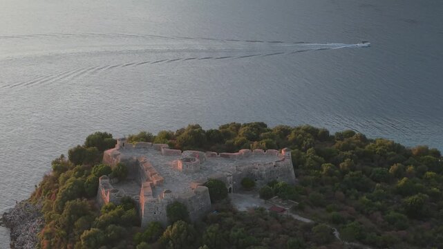 Aerial view of the historic Porto Palermo Castle situated on a peninsula surrounded by the Ionian Sea with lush vegetation and a boat nearby in Porto Palermo, Qarku i Vlores, Albania.