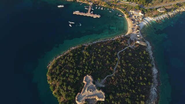 Aerial view of the turquoise waters of Porto Palermo bay with boats moored at the pier and lush green vegetation along the rocky coastline in Porto Palermo, Qarku i Vlores, Albania.
