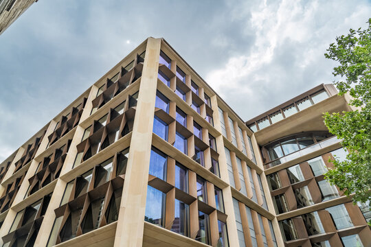 View of the Bloomberg London building featuring a modern stone and bronze grid facade with glass windows under a cloudy sky in London, England, United Kingdom.