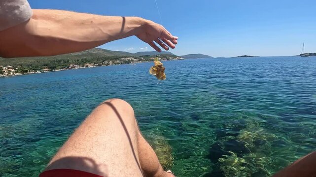 POV fisherman reeling in fishing rod and catching seaweed instead of fish. Unsuccessful fishing moment on rocky coast.