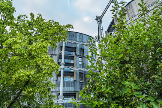 View of the Gasholders London residential building, a repurposed industrial structure with metal framework and modern balconies, framed by lush trees in London, England, United Kingdom.