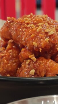 Vertical video Korean fried chicken with peanuts in spicy red sauce