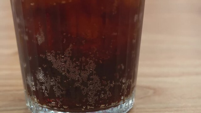 Cold cola soda with fizzy bubbles in a glass on a wooden table 4K