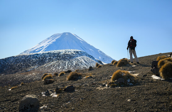 Hiking upper Tama Lake in winter.  Hiker admiring snow-capped Mount Ngauruhoe. Tama Lakes Track. Tongariro National Park. New Zealand.