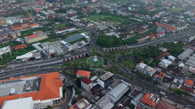 Aerial view of the Statue of Dewa Ruci at the busy roundabout intersection surrounded by urban buildings and roads in Kecamatan Kuta, Bali, Indonesia.