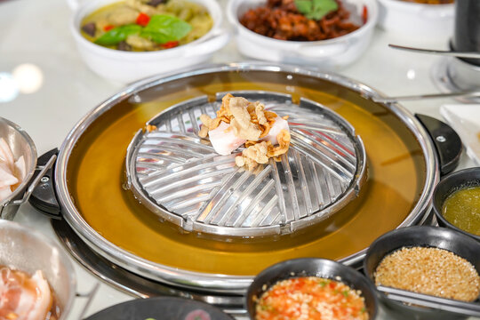 Thai Pork BBQ Buffet (Mu Kratha) &ndash; Delicious grilled sliced pork and fresh vegetables on a traditional dome skillet. Perfect for street food, Asian cuisine, and dining background graphics.