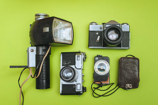 A set of rare photographic equipment. Camera, flash, film and exposure meter on a green background. Concept of obsolete film shooting and equipment. Top view, flat lay.