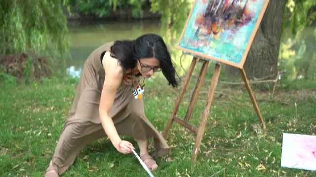 Beautiful woman artist in a dress painting on a canvas on an easel in nature by the river