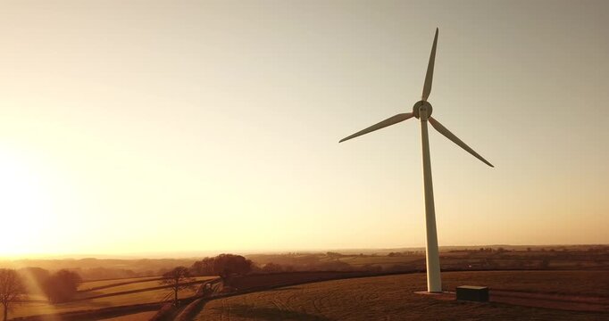 Aerial view of a wind turbine standing in a rural landscape during golden hour in Devon, England, United Kingdom.
