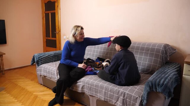 Mother and son play and joke while sorting and folding warm clothes together during an ongoing household activity.
