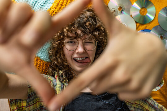 Playful teenage girl makes a hand frame while lying near a music CD