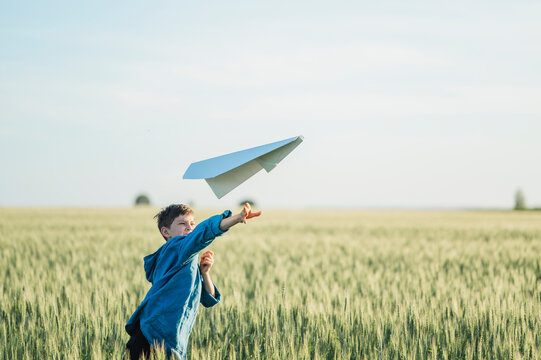 Boy throws a paper airplane in a summer field