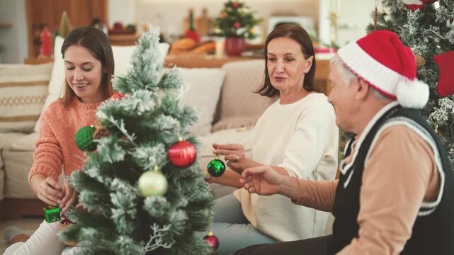 Senior couple spending Christmas with adult daughter while decorating tree, family togetherness, holiday preparation, Christmas celebration, senior family lifestyle.