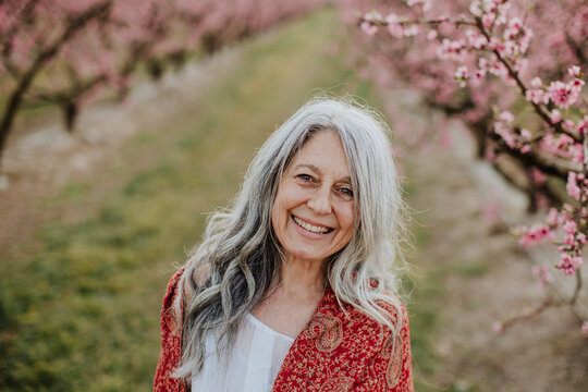 Mature woman smiles confidently in a blooming spring orchard