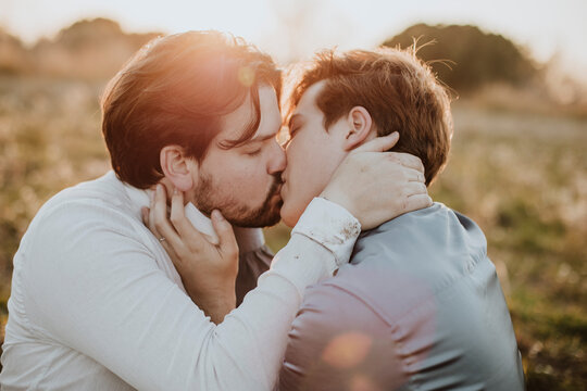 A gay couple shares a romantic kiss outdoors in a spring field