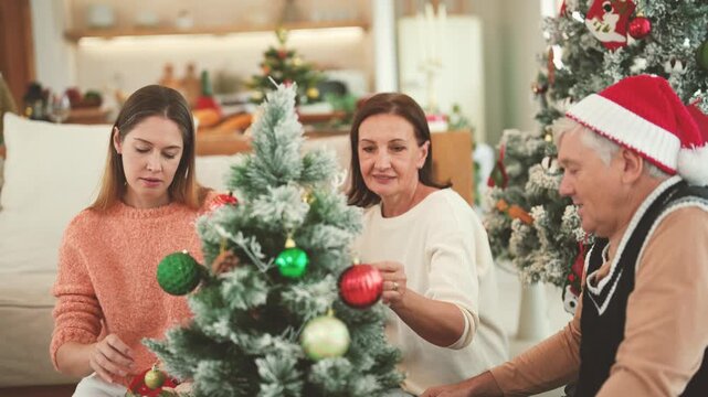 Senior parents and daughter preparing Christmas tree decorations together, multigenerational family, holiday activity, Christmas tradition, family bonding, festive celebration.