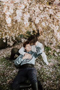 A gay couple shares a romantic embrace under a spring blossom tree