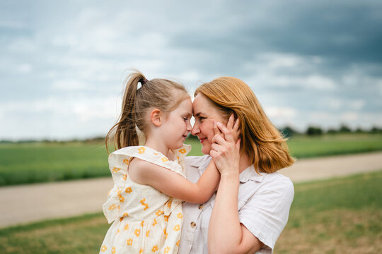 A loving mother and daughter touch foreheads outdoors