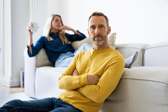 Serious man sits on the floor while woman relaxes on the sofa