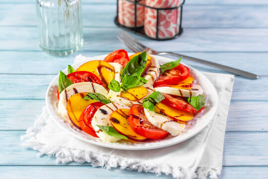 Fresh caprese salad with nectarine and tomato sits on a wooden table