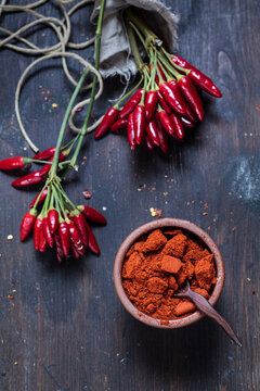 Bunches of red chili peppers and bowl with chili powder on wood