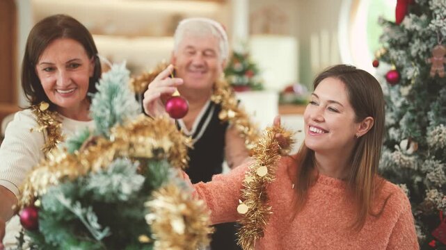 Senior parents and daughter preparing Christmas tree decorations together, multigenerational family, holiday activity, Christmas tradition, family bonding, festive celebration.