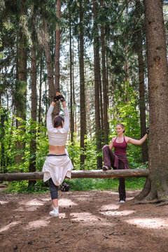 Two women perform stretching exercises on a log in the forest