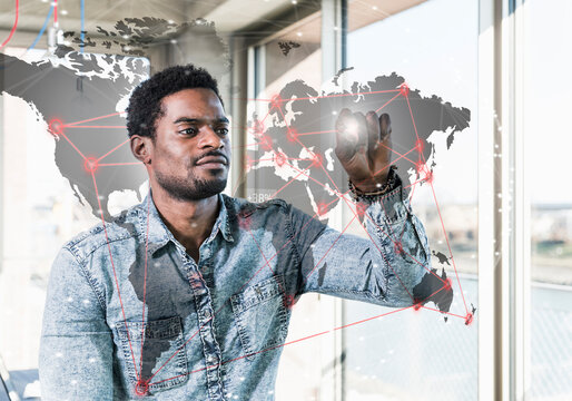 Casual businessman touching glass pane with world map in office
