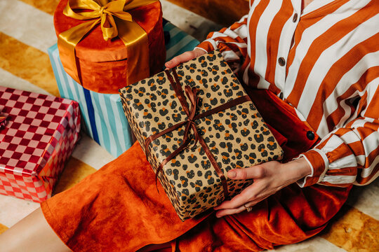 Stylish woman unwraps a vintage Christmas gift indoors on a carpet