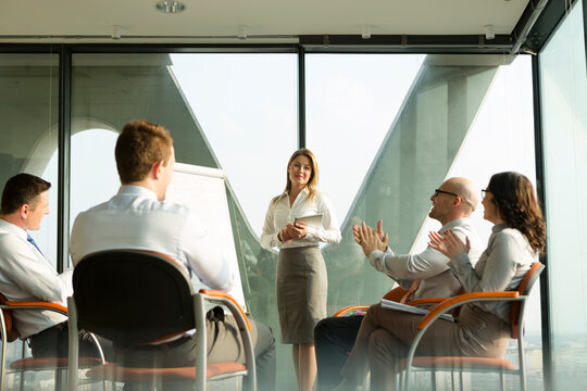 Group of businesspeople clapping hands for businesswoman at flip chart