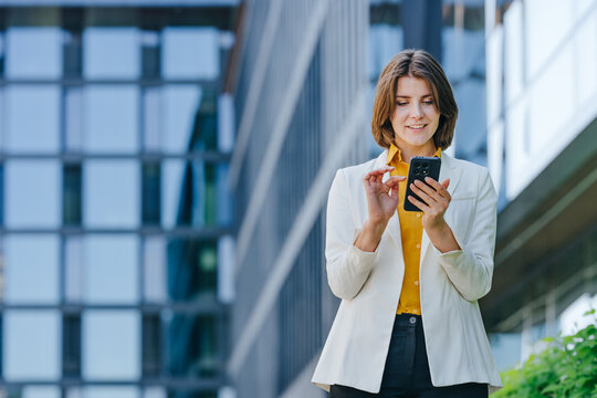 Smiling businesswoman uses phone outdoors near office building