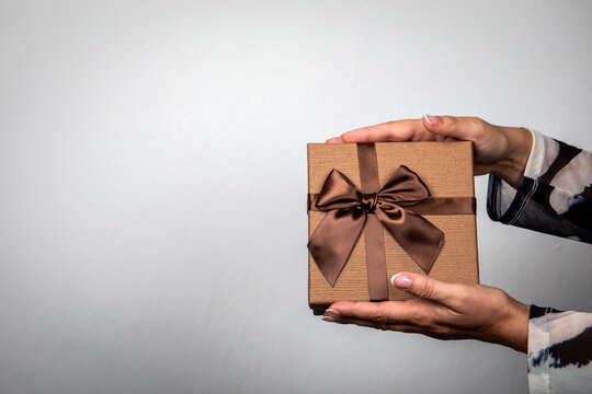 Woman Holding Elegant Gift Box With Brown Satin Bow and Copy Space
