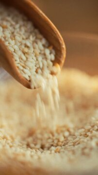 Sesame seeds tumble from a small metal scoop into a ceramic bowl on a kitchen counter, a routine step in food processing within agriculture, displaying the seed's role as a staple ingredient