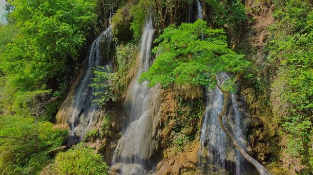 Aerial view of Sri Gethuk Waterfall with cascading water flowing over rocky cliffs surrounded by lush green tropical trees in Yogyakarta, Special Region of Yogyakarta, Indonesia.