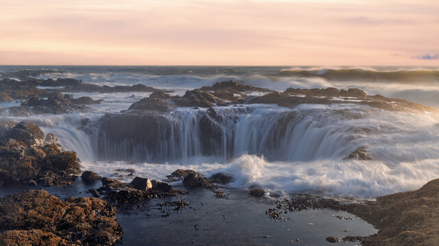 View of Thor's Well with ocean waves crashing into the rocky sinkhole during golden hour along the Pacific coastline in Yachats, Oregon, United States.