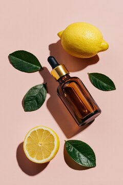 Amber dropper bottle with lemons and green leaves flatlay on pink background for natural skincare packaging and product mockup