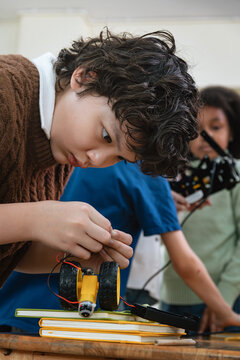 Vertical view of Generation Alpha schoolboy concentrates on assembling small robot wheels during focused hands on STEM classroom activity at primary school, showing cognitive learning and development