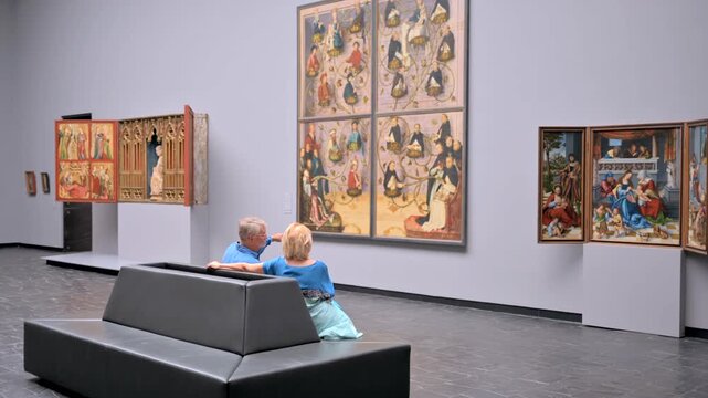 Elderly couple observing ancient renaissance paintings in quiet museum gallery.