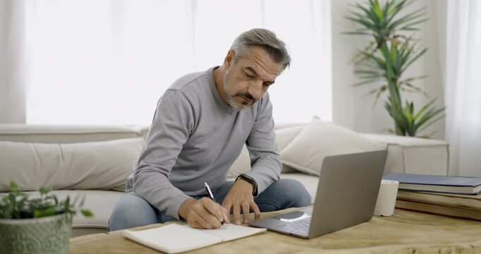 Portrait of senior old caucasian man stay home sit on the sofa  living room working on computer write a note. Happy moment of pure love middle age male work from home or distance workspace